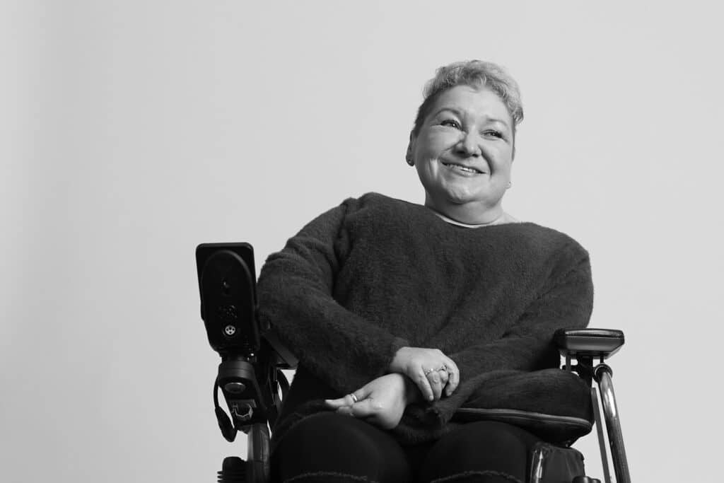 A black & white photo of Clare Gray in her wheel chair smiling. photo credit the Shaw Trust